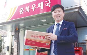 홍북우체국 앞에서 택배상자를 들고 포즈를 취한 이형균 우체국장,