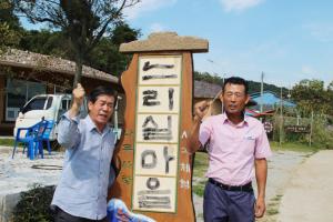 김찬 총무(왼쪽)와 이춘학 이장이 느리실마을 현판 앞에서 포즈를 취하고 있다.