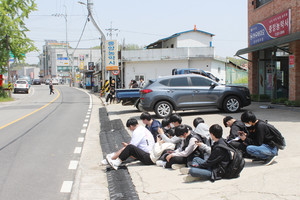승강장 없이 바닥에 앉아 버스를 기다리고 있는 갈산고등학교 통학생들의 모습이 위태로워 보인다.