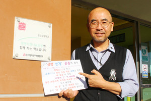 &nbsp;‘생명 잇기’ 운동의 취지가 적혀있는 인쇄물을 들고 웃고있는 김한정수 교사.