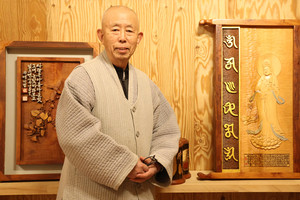 부조와 서각이 어우러진 작품 앞에서 지법 스님이 미소짓고 있다.
